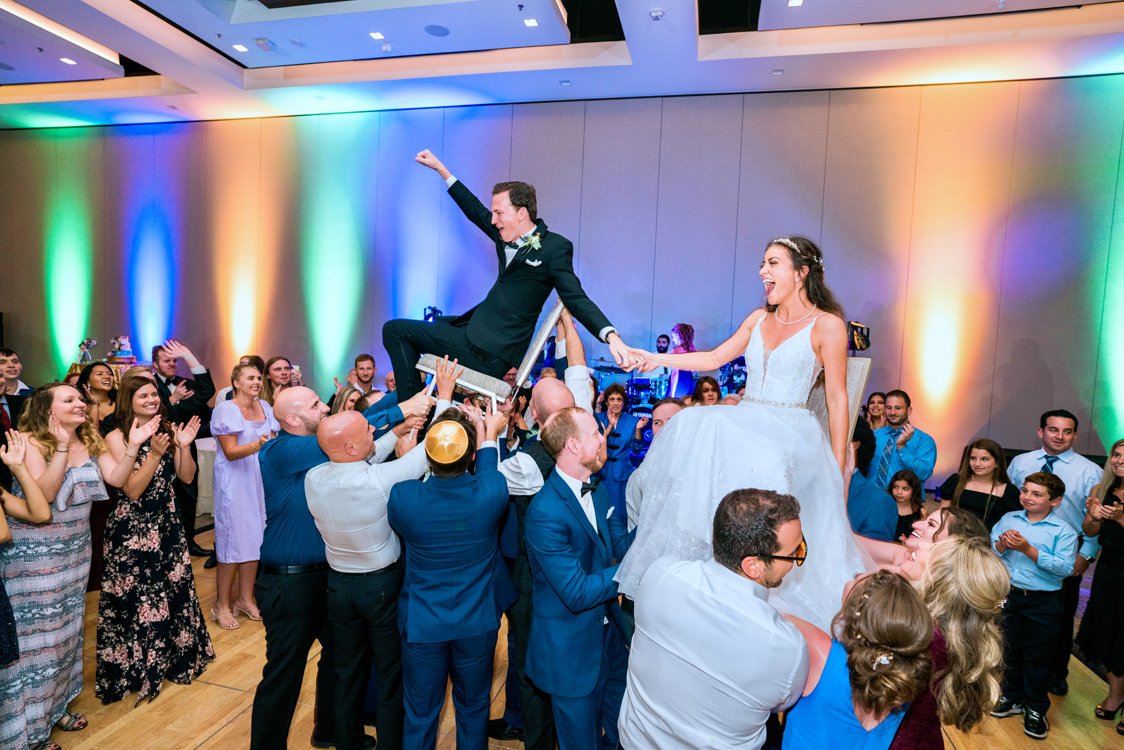 Bride and groom lifted during the hora dance surrounded by cheering guests at an elegant wedding reception