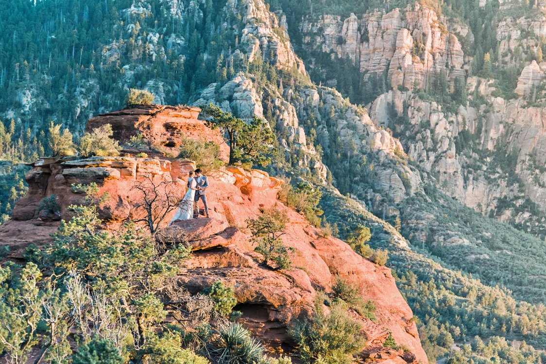 Bride and groom embrace on Sedona red rock cliffs at sunset during destination wedding shoot