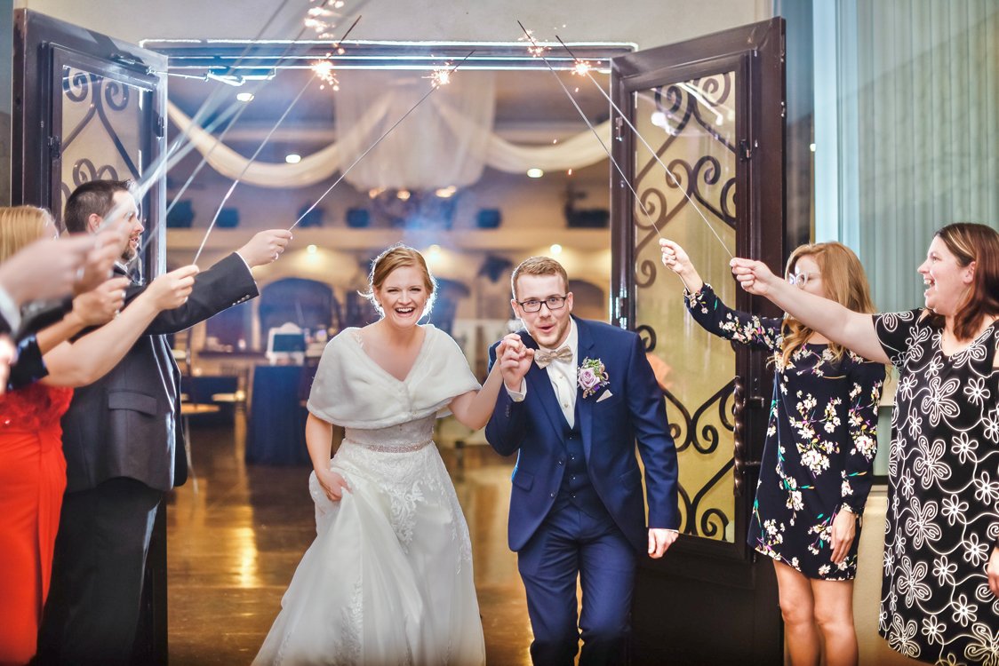 Bride and groom running through sparkling exit tunnel surrounded by cheering wedding guests