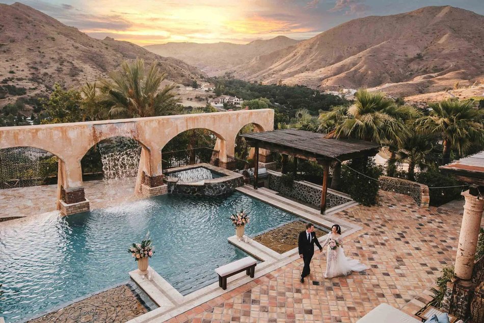 Mediterranean Private Estate With Arched Waterfall Hillside estate courtyard with arches, pool, and terracotta pavers at sunset.