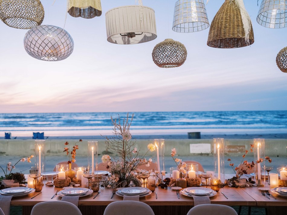 Sunset Beach Reception in San Diego with Woven Lanterns Intimate oceanfront reception table at dusk in San Diego with woven pendant lights and candles.