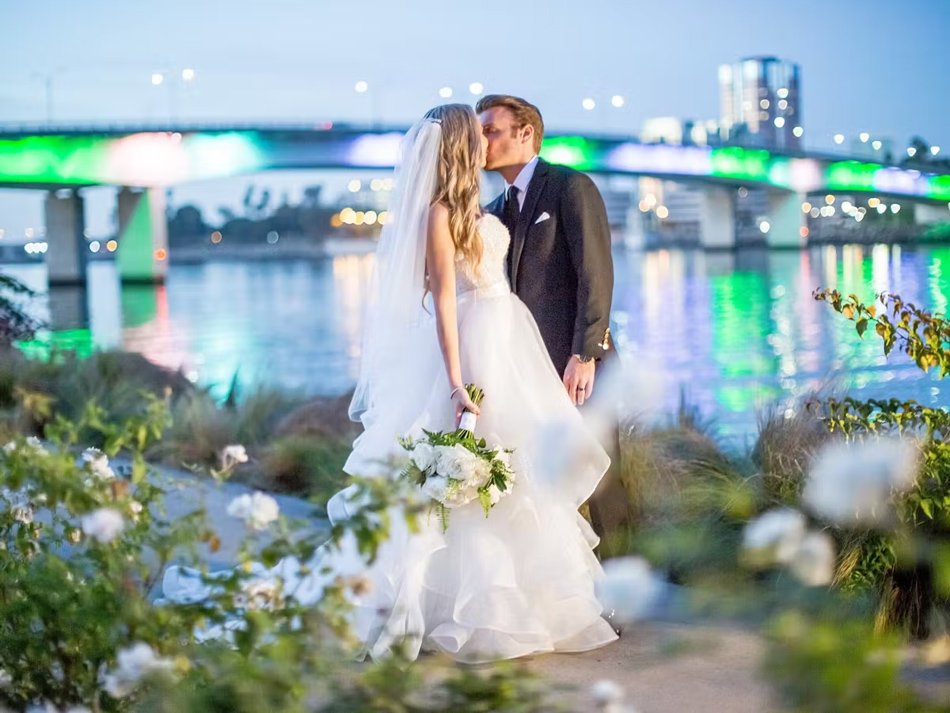 Bride and groom kiss by the water at Hotel Maya in Long Beach, Los Angeles County—city lights reflecting across the bay for a chic Southern California vibe.