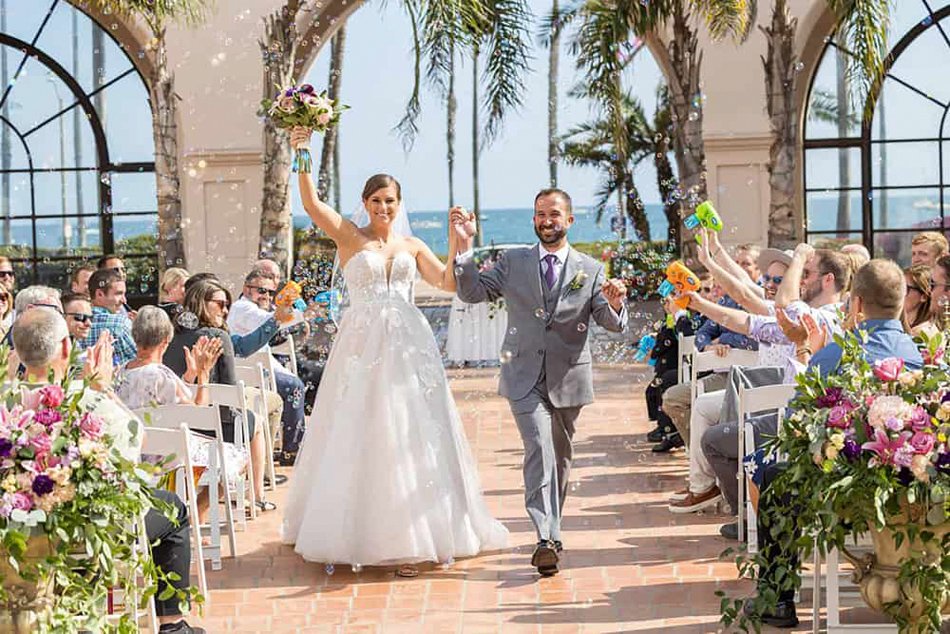 Newlyweds exit an oceanfront ceremony at Hilton Santa Barbara Beachfront Resort with bubbles, palms, and Pacific Ocean views — Southern California.