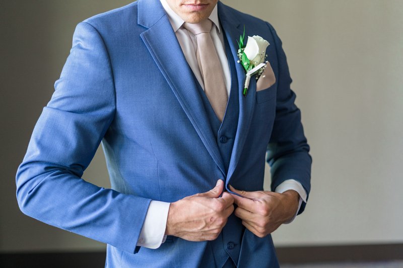 Groom in a blue suit fastening jacket with white boutonniere
