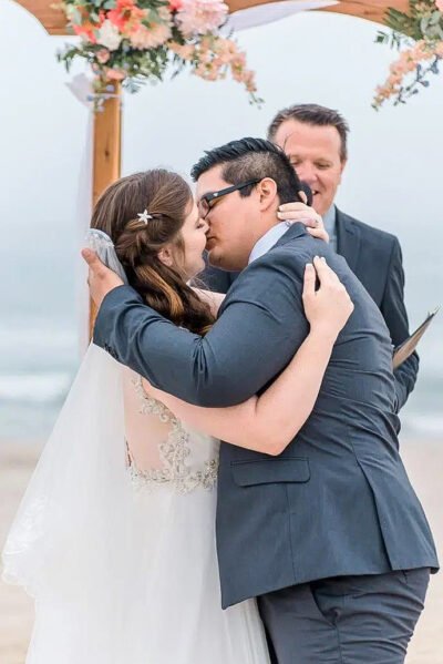 Groom watching bride walk down the beach aisle