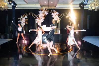 Luxury South Asian wedding reception with dancers performing on a reflective black dance floor and tall floral arches.