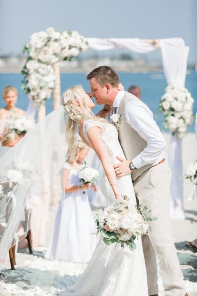 Seaside ceremony kiss under white florals — Southern California beach — Lovelee Photography