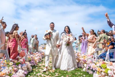 Bride and groom walking back up the aisle after their outdoor coastal wedding ceremony, surrounded by wedding party and pastel florals.