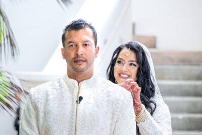 Romantic indoor first look of a South Asian bride and groom facing each other and laughing.