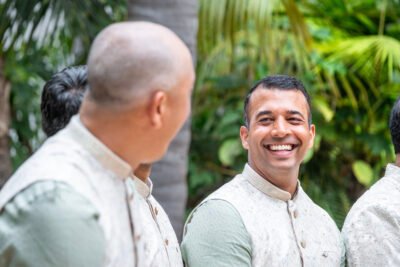 Groom laughing with a groomsman in coordinated ivory sherwanis before the wedding ceremony.