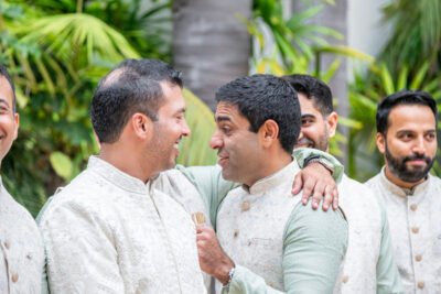 Groom laughing with a groomsman in coordinated ivory sherwanis before the wedding ceremony.