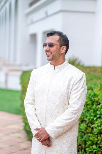 South Asian groom in an ivory sherwani smiling during a portrait on the resort lawn.