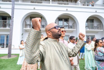 Guest cheering with arms raised during outdoor wedding celebration at a white resort.