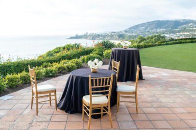 Oceanfront cocktail hour setup with black linens and gold chairs overlooking the coastline.