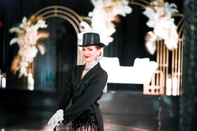 Cabaret performer in a black suit and top hat smiling on stage at a luxury wedding reception.