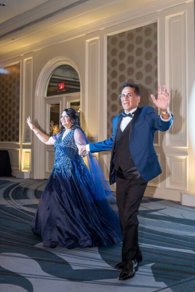 Bride in a flowing blue gown and groom in a tuxedo making a joyful entrance into the reception.