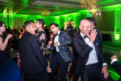 Wedding guests dancing and laughing on a packed dance floor with vibrant green uplighting.