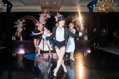 Bride and groom on stage during a reception performance with glamorous showgirls and dramatic lighting.